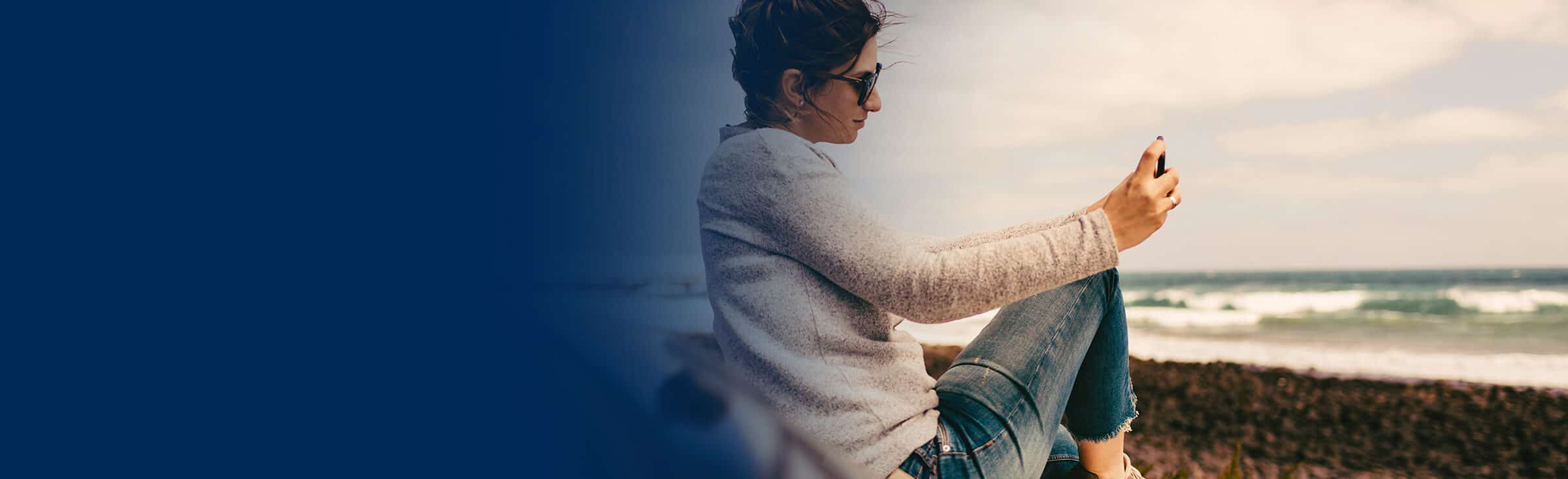 Woman sits on the beach looking at her phone